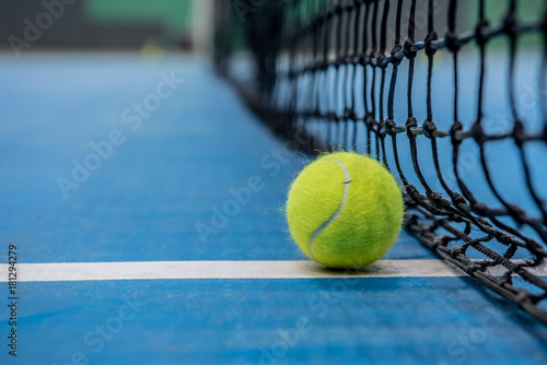 Yellow tennis ball on blue hard court surface with black net