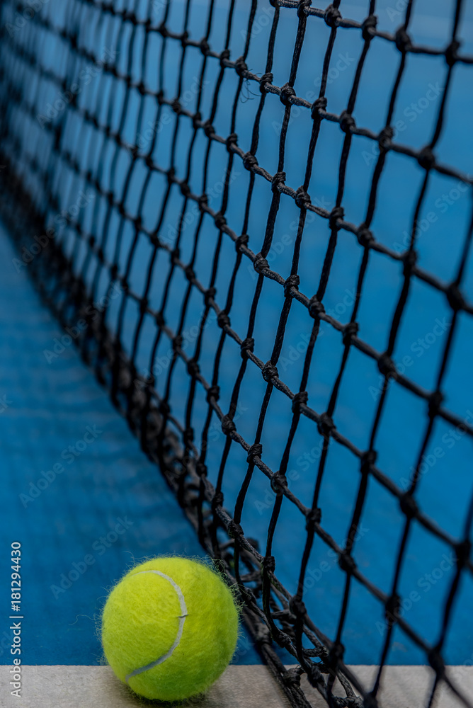 Yellow tennis ball on blue hard court surface with net in background
