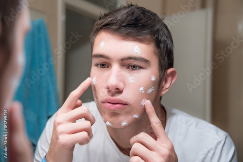 Young attractive man applying acne cream on face
