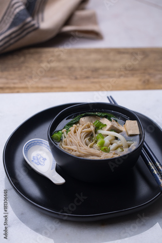 Japanese udon noodle soup with enoki mushroom, tofu and Gai lan. Black ceramic bowl and a plate 
