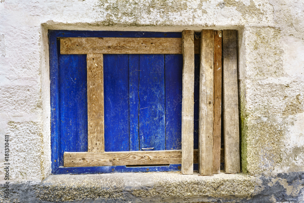 Walled window with a blue board and unpainted horizontal and vertical timbers in the frame of a very old stone house