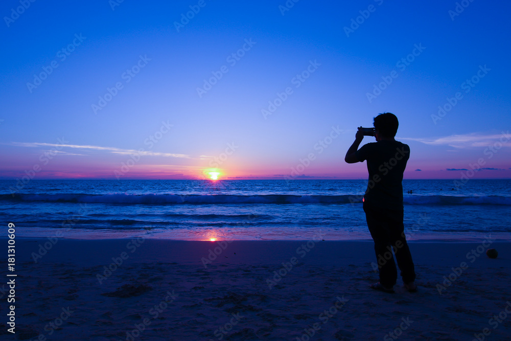 silhouette man on the beach taking the photo with his mobile during sunset at Phuket Thailand