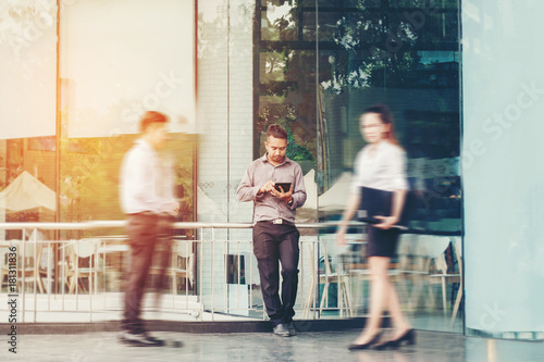 Businessman using a digital tablet office outdoors and Blurred People Walking in Front of Modern Office Building photo