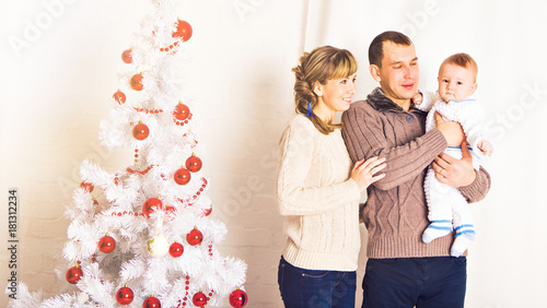 Happy parents with baby in decorated room for Christmas photo