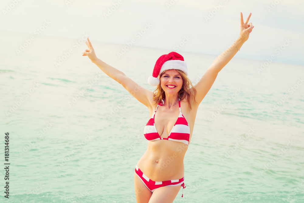 Happy woman in Santa hat enjoying winter vacation on the beach
