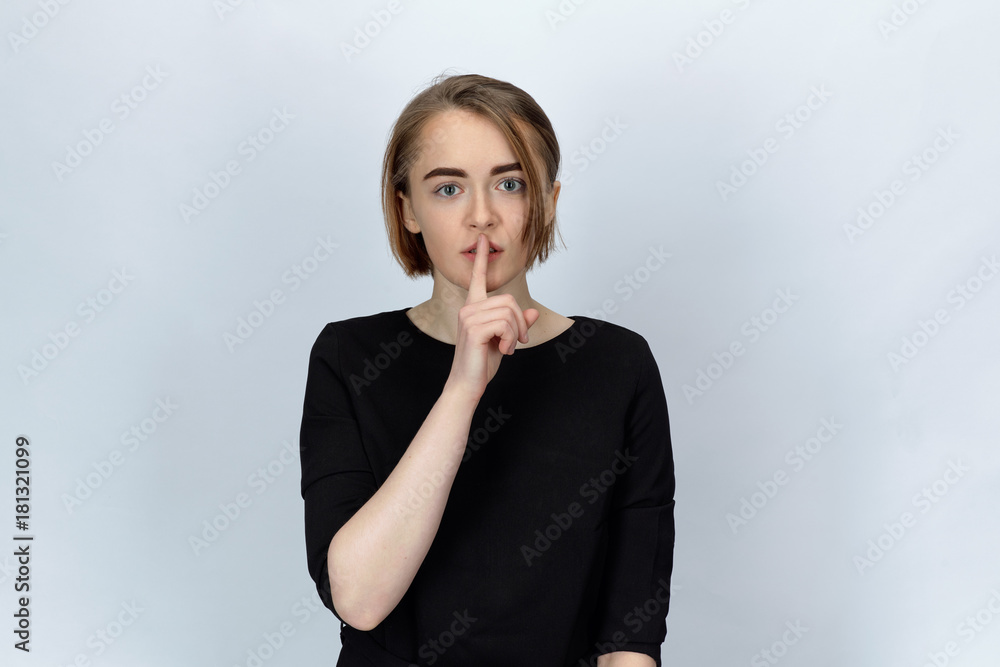Studio portrait on isolated background of a young attractive woman with wide open eyes, holding a finger to call for silence Studio portrait on isolated background of a young attractive woman with wide open eyes, holding a finger to call for silence