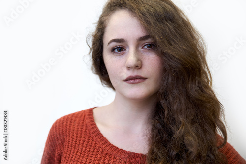 close-up portrait on a white background in natural light skinned, freckled young attractive girl woman with long red curly hair dressed in a red sweater © EverGrump