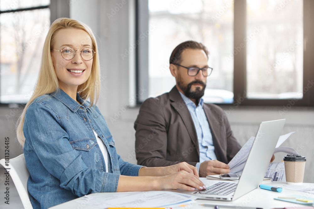 Obraz premium Female and male economists work with documents and modern technologies, sit over modern office interior, busy all day. Team of professional leaders prepare monthly report on business meeting