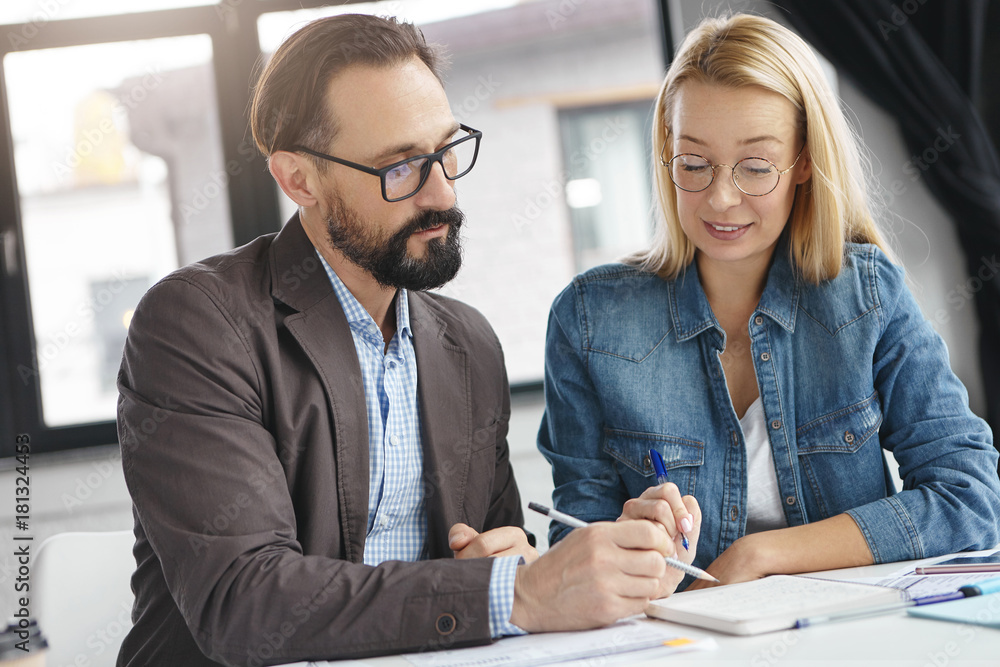 Successful man and woman discuss current issues or business strategy at modern office builduing. Two corporate workers involved in working process, focused at notebook with notes, write something Successful man and woman discuss current issues or business strategy at modern office builduing. Two corporate workers involved in working process, focused at notebook with notes, write something
