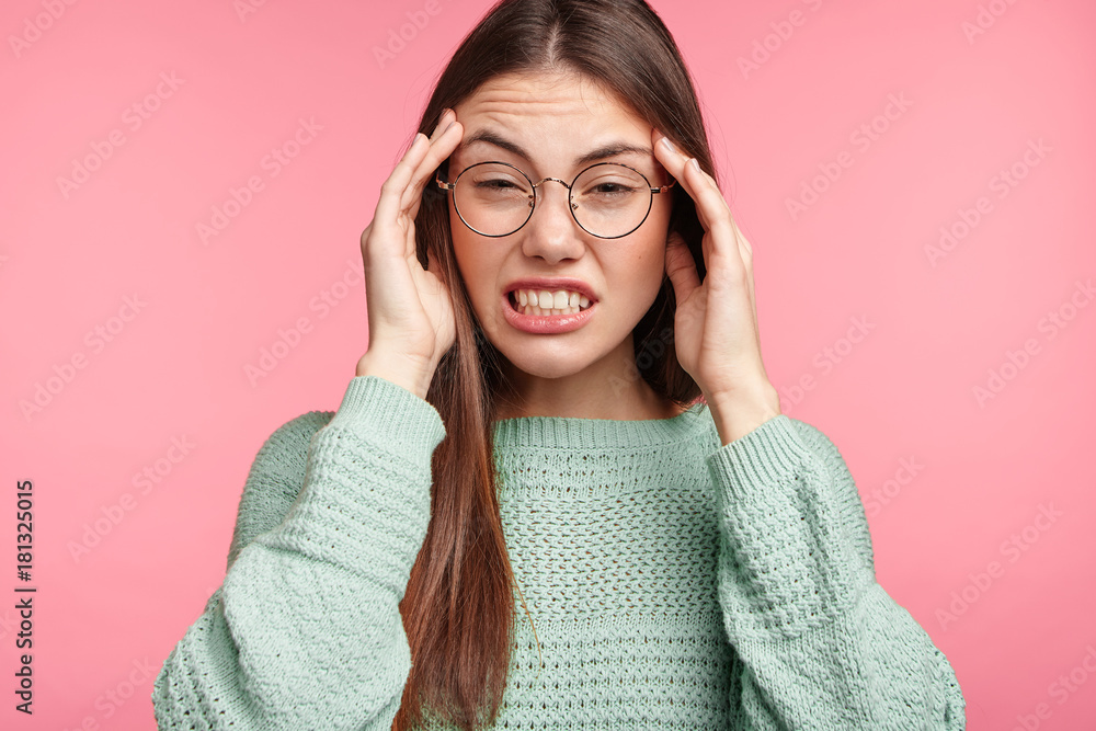 Horizontal portrait of brunette Asian female has headache after noisy party, clenches teeth and holds hands on temples. Disappointed young female worker overworked after making advertising content Horizontal portrait of brunette Asian female has headache after noisy party, clenches teeth and holds hands on temples. Disappointed young female worker overworked after making advertising content