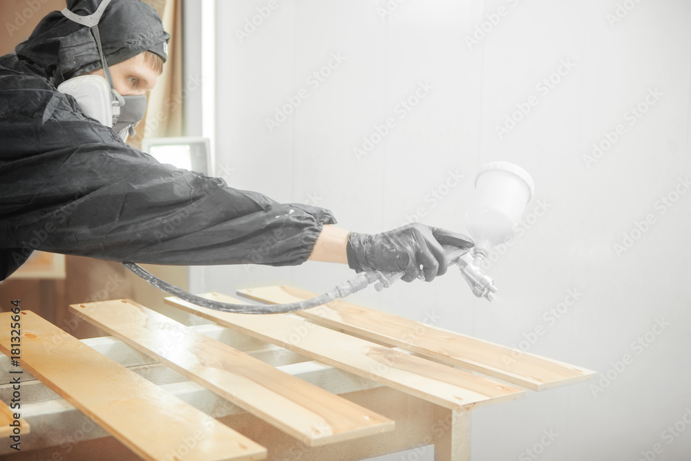 Man in respirator mask painting wooden planks at workshop. Man in respirator mask painting wooden planks at workshop.