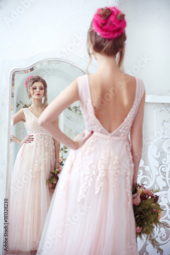 Elegant bride with a bouquet in hand in front of the mirror view from the back. © ksi