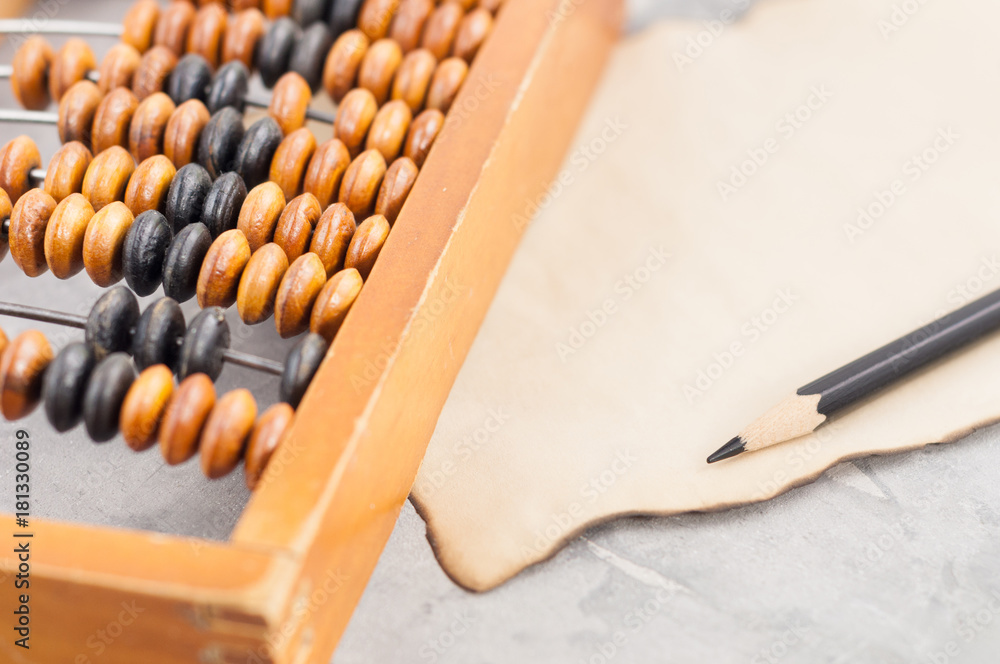 Old wooden abacus beside burnt paper and black pencil on cracked gray concrete Old wooden abacus beside burnt paper and black pencil on cracked gray concrete