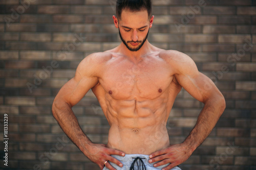 Young athlete posing with a torso for photography on a brick wall background. Bodybuilder, athlete with pumped muscles, breast and arm rescue