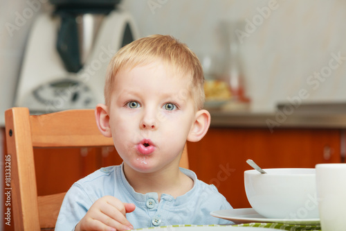 Kid boy eating breakfast, cereals and milk in bowl