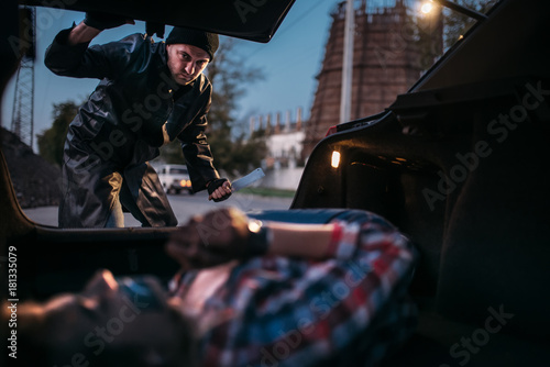 Serial maniac looks on female victim in car trunk © Nomad_Soul