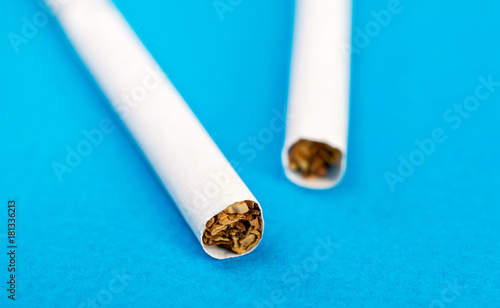 Two cigarettes on a blue background. Close up.