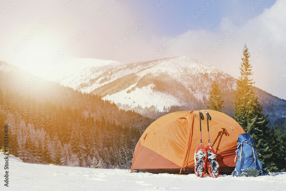 Winter trek in the mountains. The tent stands on the mountainside against the backdrop of the mountains.