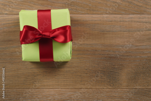 green paper gift box with red ribbon bow on oak table