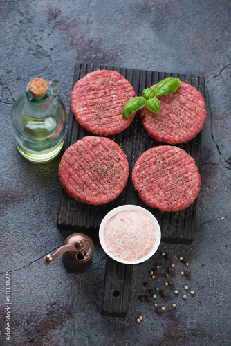 Black wooden cutting board with raw seasoned beef burgers on a weathered asphalt background, high angle view, studio shot