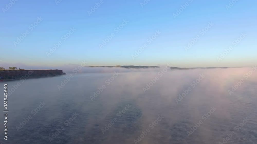 AERIAL: A thick fog over the lake at dawn. Steep shore, beautiful soft light, camping on the shore, travel, weekends, rest. Amazing landscape. AERIAL: A thick fog over the lake at dawn. Steep shore, beautiful soft light, camping on the shore, travel, weekends, rest. Amazing landscape.