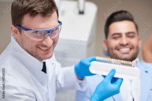 Professional dentist smiling to the camera while working with his patient holding dentures choosing matching color for his patient copyspace professionalism occupation healthcare medicine dentistry.