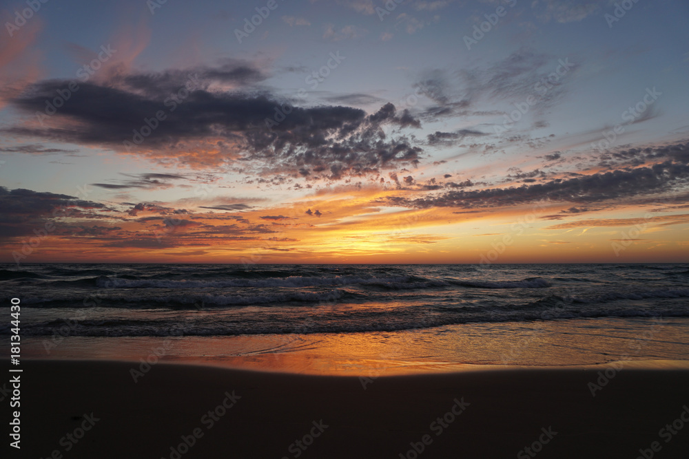 Sunset at the beach with waves on shore reflecting sky.