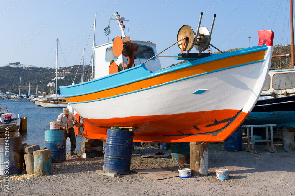 Patmos island, Greece - August 22nd 2017 - An old man is repairing his fishing boat in the harbor of Patmos Patmos island, Greece - August 22nd 2017 - An old man is repairing his fishing boat in the harbor of Patmos