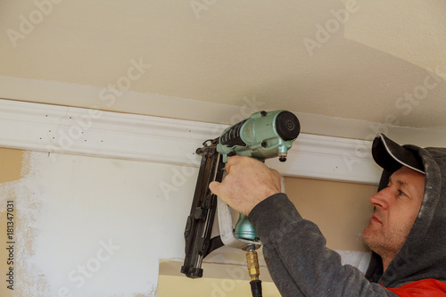 Carpenter brad using nail gun to Crown Moulding trim, warning label that all power tools photo