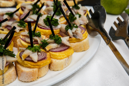 One plate with snacks on a buffet table. Selection of tasty bruschetta or canapes on toasted baguette with potatoes herring fish, red onions. photo