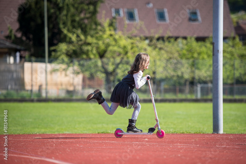 Little girl riding a scooter on a sports facility