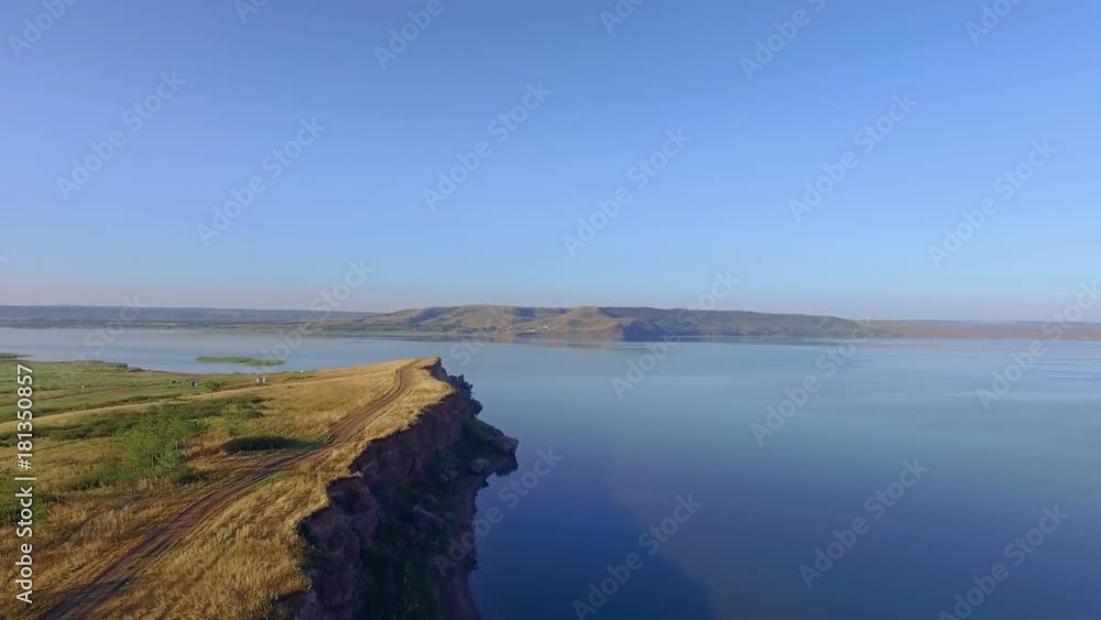 AERIAL: View from above on the huge lake with rocky coast. End of summer, yellowed grass, blurred hills on the horizon. Beautiful sunrise scenery. AERIAL: View from above on the huge lake with rocky coast. End of summer, yellowed grass, blurred hills on the horizon. Beautiful sunrise scenery.