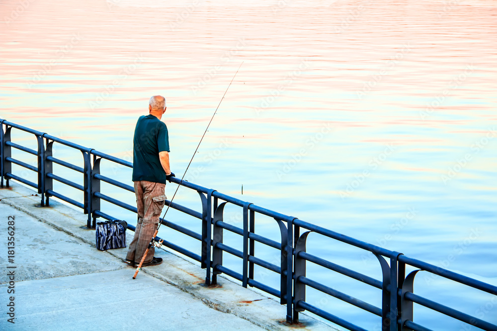 A fisherman stands on the river bank with a fishing rod.