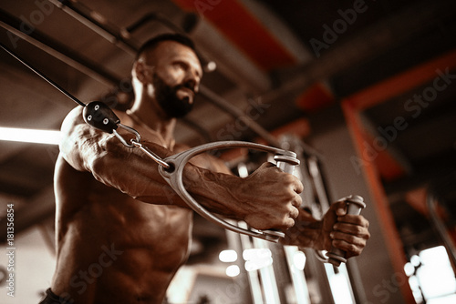 Handsome man with big muscles working out in gym. Muscular bodybuilder doing exercises.
