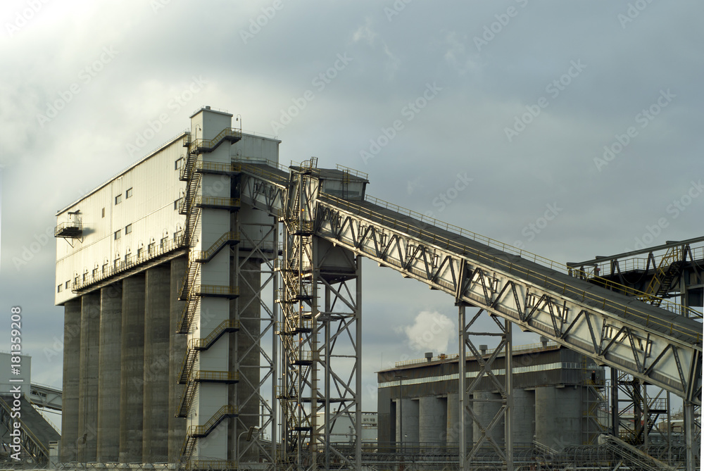 fragment of a modern industrial enterprise with silos for storage of loose materials and an inclined covered belt conveyor..