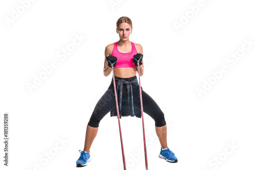 Strong woman using a resistance band in her exercise routine. Young woman performs fitness exercises on white background.