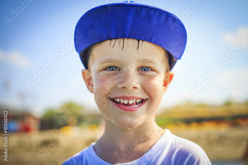 Portrait of happy caucasian boy in cap with wet drops on his face. The face of smiling boy after bathing on bright sunny summer day © dzmitrock87