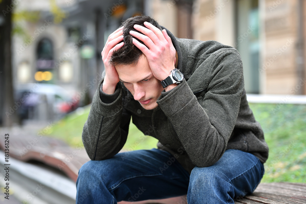 young sad man thinking while sitting on a bench in autumn young sad man thinking while sitting on a bench in autumn