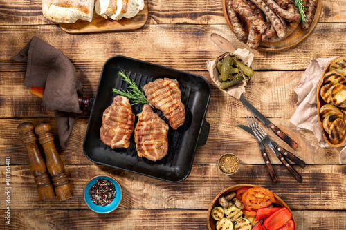barbecued steak, sausages and grilled vegetables on wooden picnic table