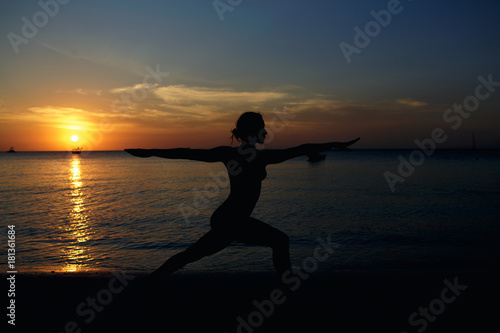 Silhouette of woman practicing yoga on ocean coast at sunset