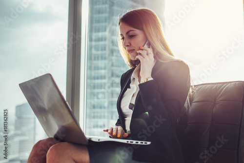 Billede på lærred Young woman waiting in a hall sitting in modern office working on laptop talking