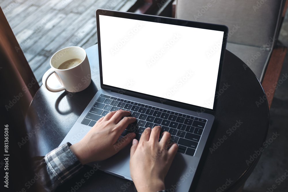 Mockup image of business woman using and typing on laptop with blank white screen and coffee cup on wooden table in cafe Mockup image of business woman using and typing on laptop with blank white screen and coffee cup on wooden table in cafe