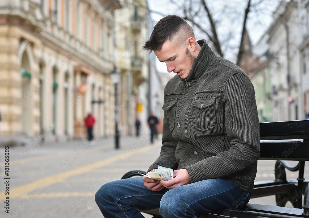 young man sitting on a bench and counting money young man sitting on a bench and counting money