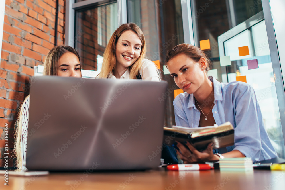 Three young girlfriends talking online lesson using a laptop sitting in a library Three young girlfriends talking online lesson using a laptop sitting in a library