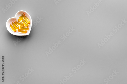 Treat heart. Pills in bowl in shape of heart on grey background top view copyspace photo