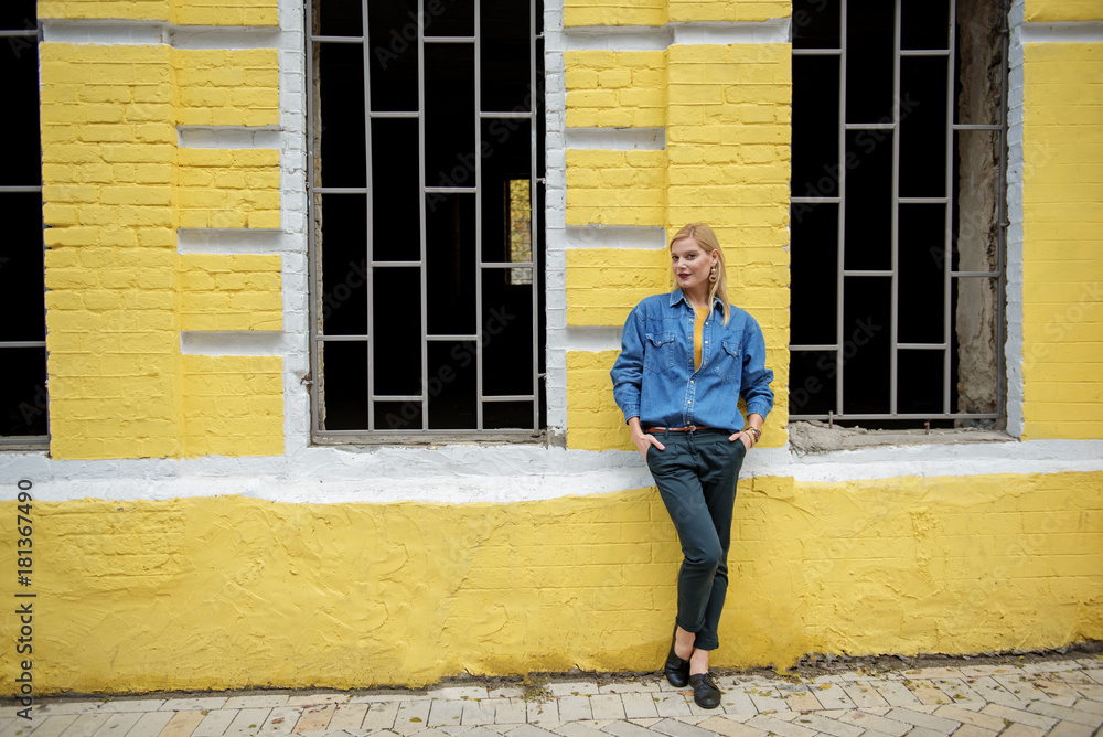Full length portrait of confident blond girl standing near yellow building outdoor and posing. Copy space Full length portrait of confident blond girl standing near yellow building outdoor and posing. Copy space