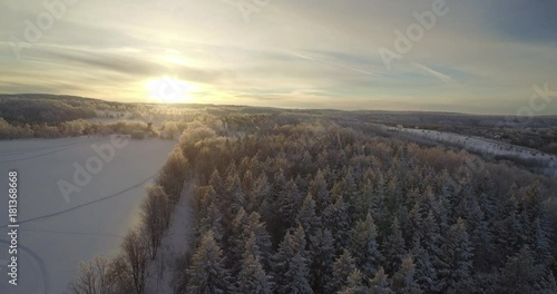 A zoom out of the sun rising over some trees with snow on the ground