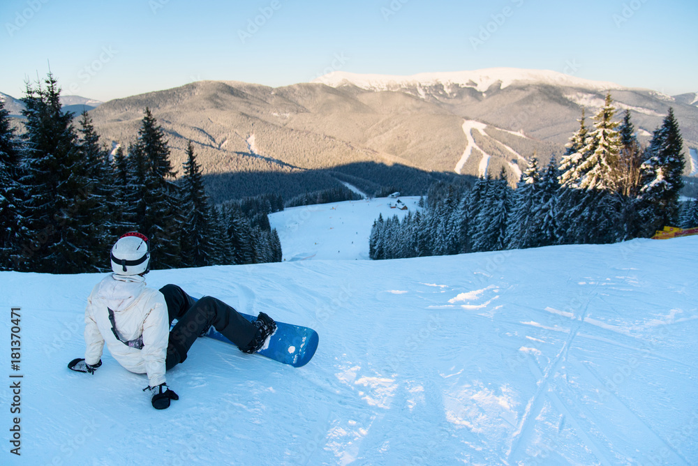 Woman with a snowboard sitting on the fresh snow top of a mountain enjoying  the scenery