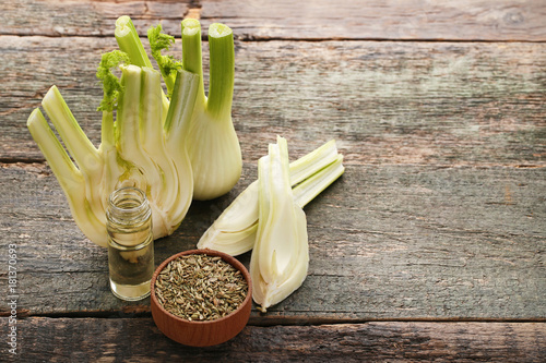 Ripe fennel bulbs with dry seeds in bowl and bottle of oil on blue wooden table