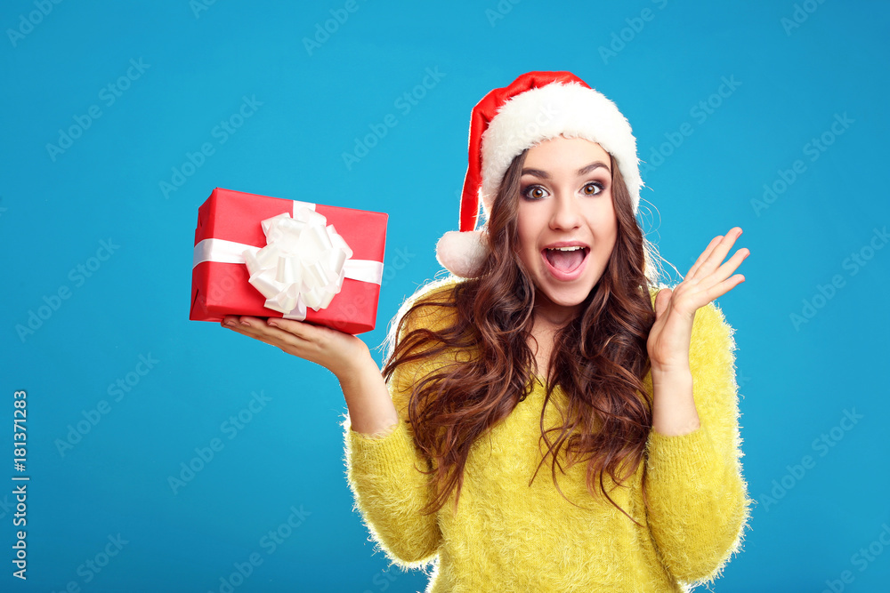 Obraz premium Beautiful young girl holding gift box on blue background